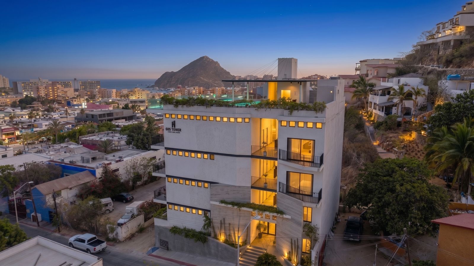 605 Tower — boutique building in downtown Cabo San Lucas at dusk, with the marina and Land's End beyond