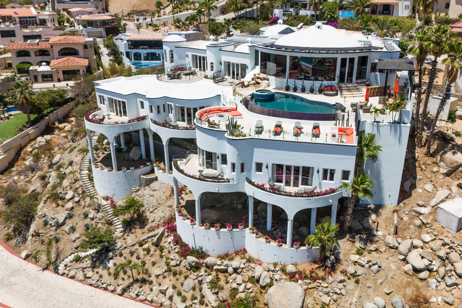Aerial view of Casa Buzzard — multi-level white compound cascading down rocky hillside with multiple terraces and rooftop pool