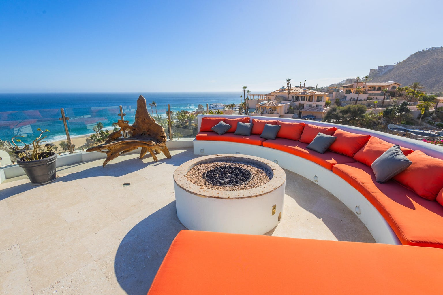 Rooftop fire pit lounge with curved terracotta cushioned seating, driftwood sculptures, panoramic ocean views