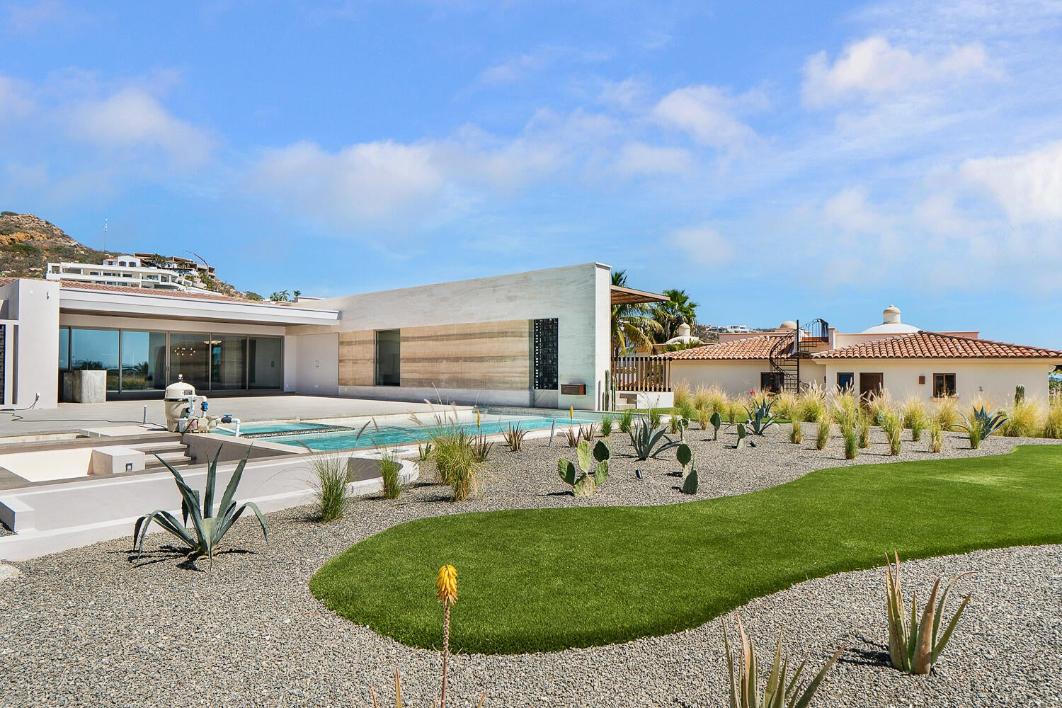 Desert-modern landscaping with native agave, ornamental grasses, cacti, gravel garden, lap pool, manicured lawn, and mountain backdrop